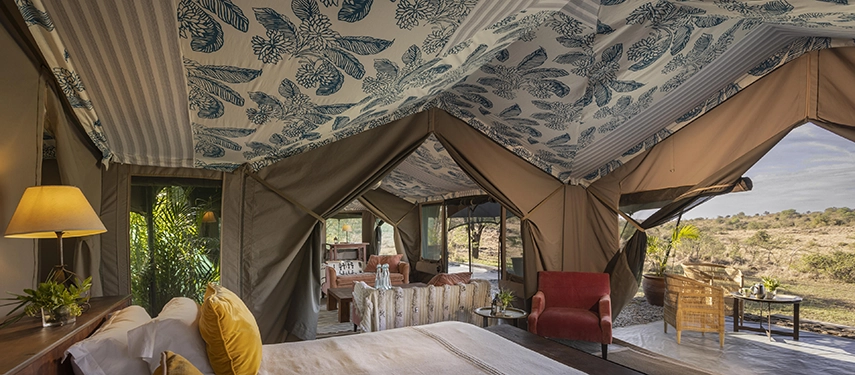 A sun-filled Family Tent interior at Hemingways River Camp Mara, with a king bed, bold botanical canvas ceiling and open sides revealing the open Mara plains.