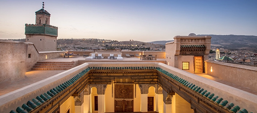 Expansive rooftop terrace at Dar Bensouda at twilight with panoramic views of the medina and surrounding hills.