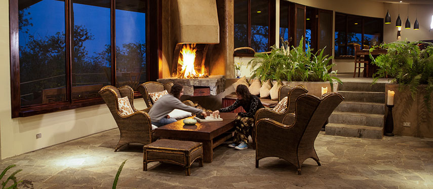 A couple relaxes in the cosy guest lounge and fireplace at Galápagos Safari Camp
