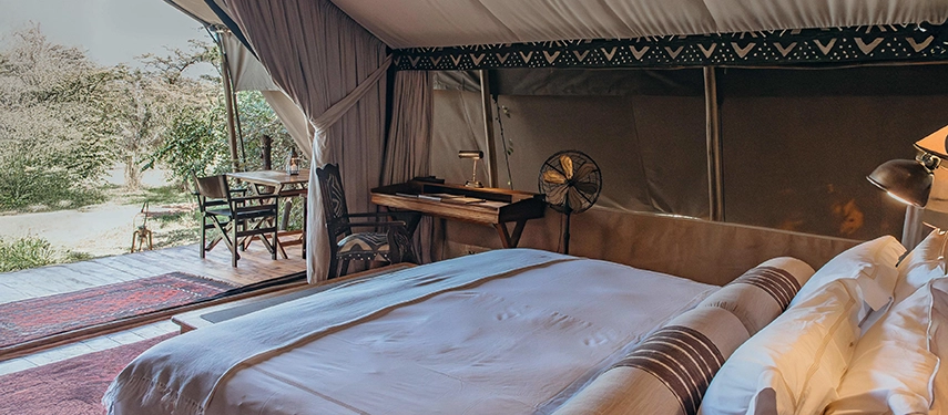Interior view of a Mara Expedition Camp safari tent in Kenya, opening onto a private deck with views across the Maasai Mara landscape.