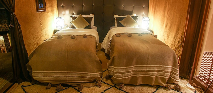 Twin beds with soft throws and Moroccan lanterns inside a luxury desert tent.