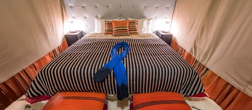 Spacious desert tent with a double bed dressed in striped linens and vibrant cushions.