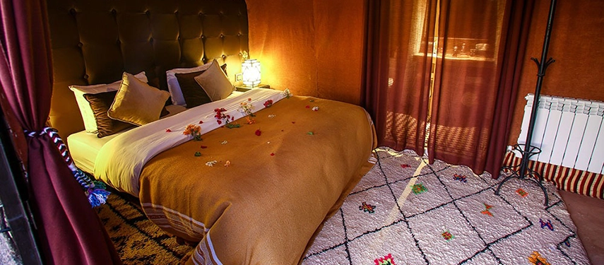 Romantic desert tent bedroom with double bed decorated with flower petals and warm lighting.