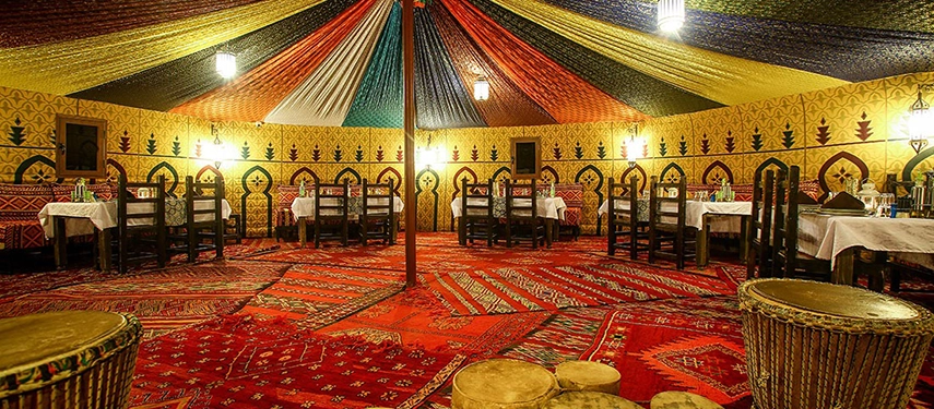 Spacious Berber dining tent with colourful carpets, patterned walls, and traditional seating.