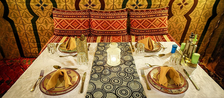 Elegant dining table in a Berber-style tent set with patterned plates, lantern, and traditional décor.