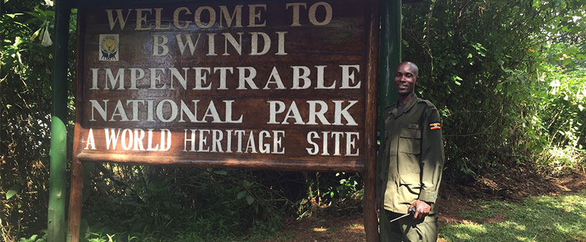 Guide stands by the welcome sign to Bwindi Impenetrable Forest