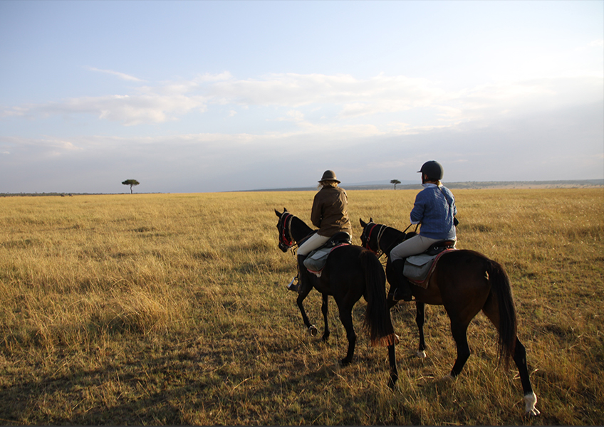 Two people horse riding across the Masai Mara