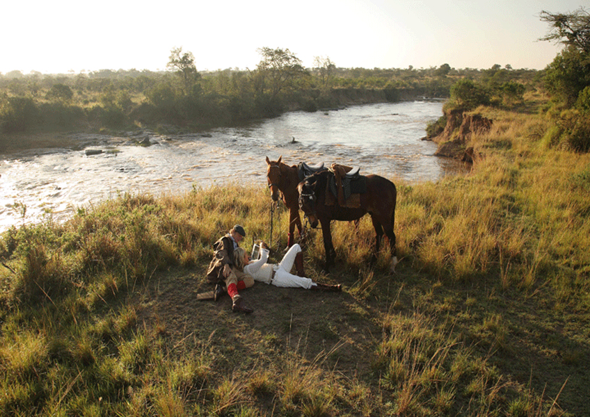 A couple lie by a river in a romantic setting on an African riding safari in Kenya