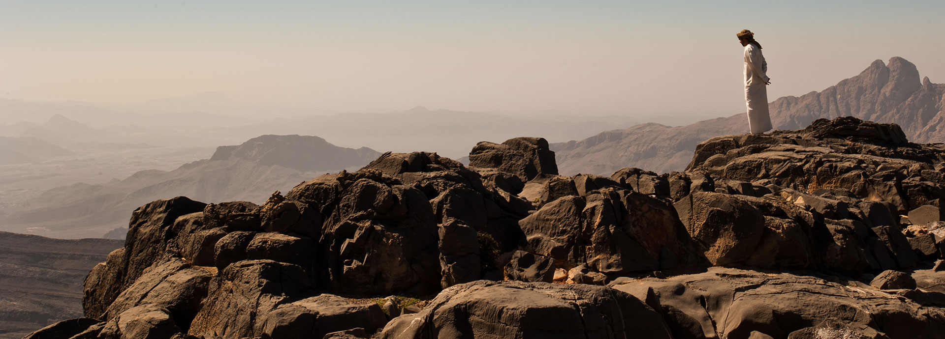 A man wearing traditional clothing standing on the edge of a vast canyon on Oman