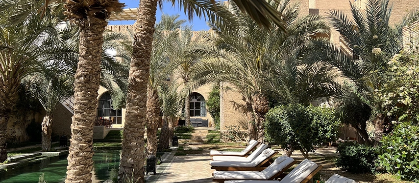 Palm-shaded poolside at Dar Tozeur with cushioned sun loungers and traditional brick architecture.