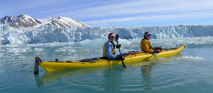 A couple kayaking amongst icebergs with a glacier in the background