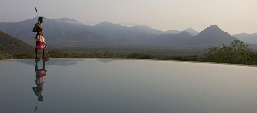 Samburu tribesman walking along the edge of an open-air swimming pool with incredible views across Kenya's Mathews Range.