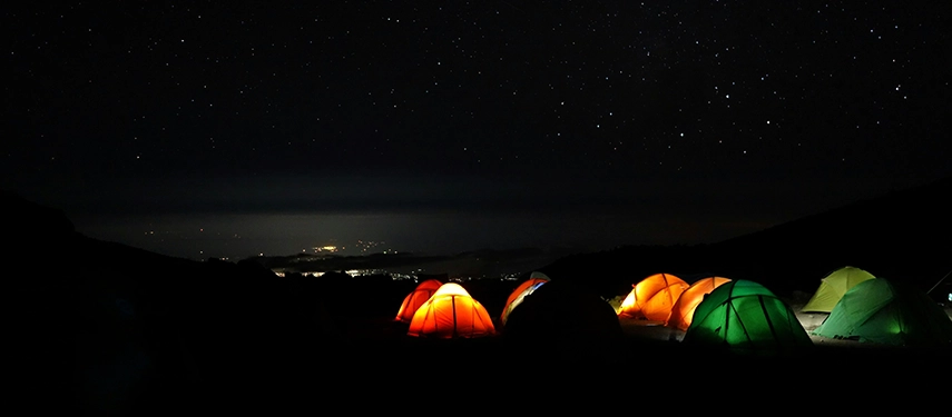 Cluster of glowing tents beneath a starry sky at a high-altitude campsite on Mount Kilimanjaro.