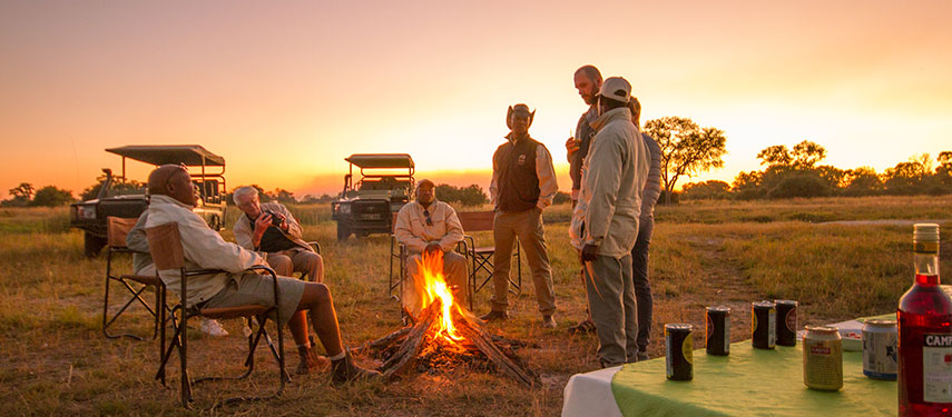 Share stories around the campfire while the sun sets behind you at Kwando Lebala Camp in Botswana