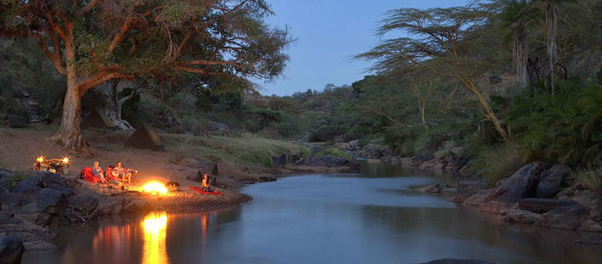 Guests at Ol Malo gathered around a campfire on the banks of a river