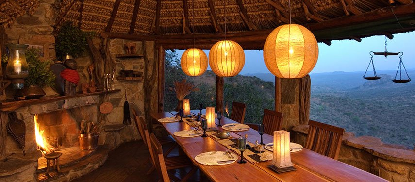 Lamp-lit dining room with inviting open fire and views across Kenya's Ol Malo Reserve