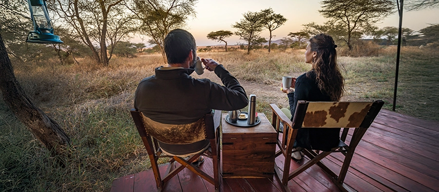 Couple enjoying morning coffee on a private deck overlooking the African savannah at Lewa Safari Camp.