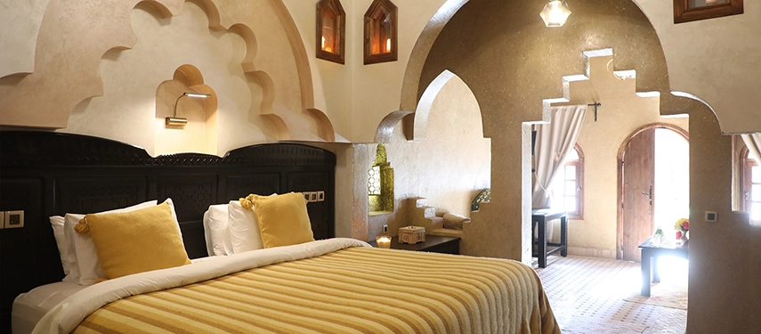Spacious Moroccan suite with arched alcoves, golden striped bedding, and traditional architectural details.