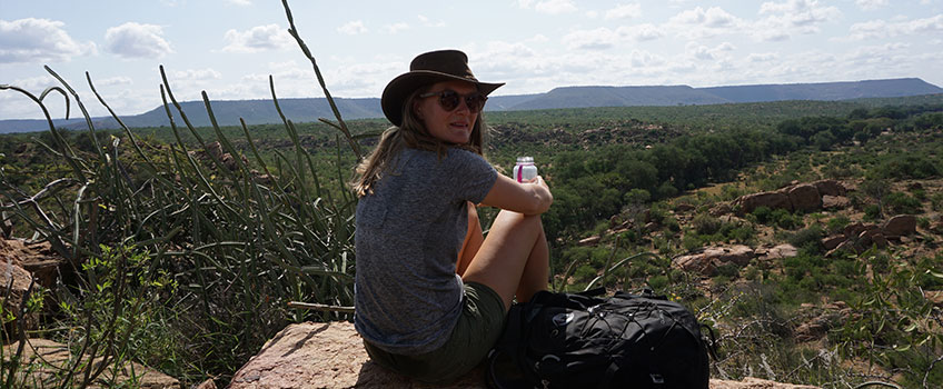 A walker takes a pause on a rock overlooking the African wilderness