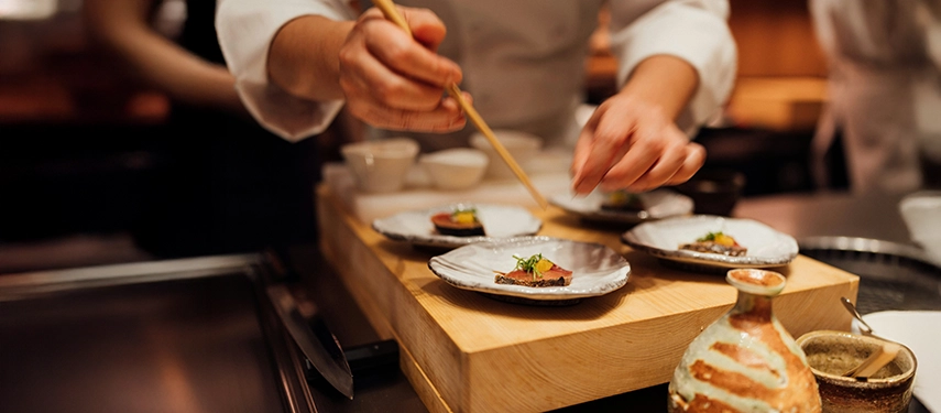 A Japanese chef delicately plates seasonal dishes at a traditional counter, highlighting precision, craftsmanship and refined culinary culture.