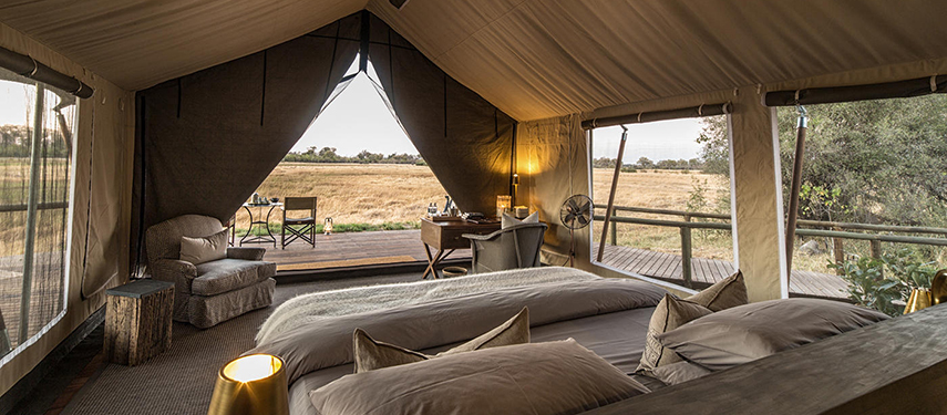 Interior of a luxury canvas tent with twin beds, writing desk, and deck chairs overlooking the golden savannah.