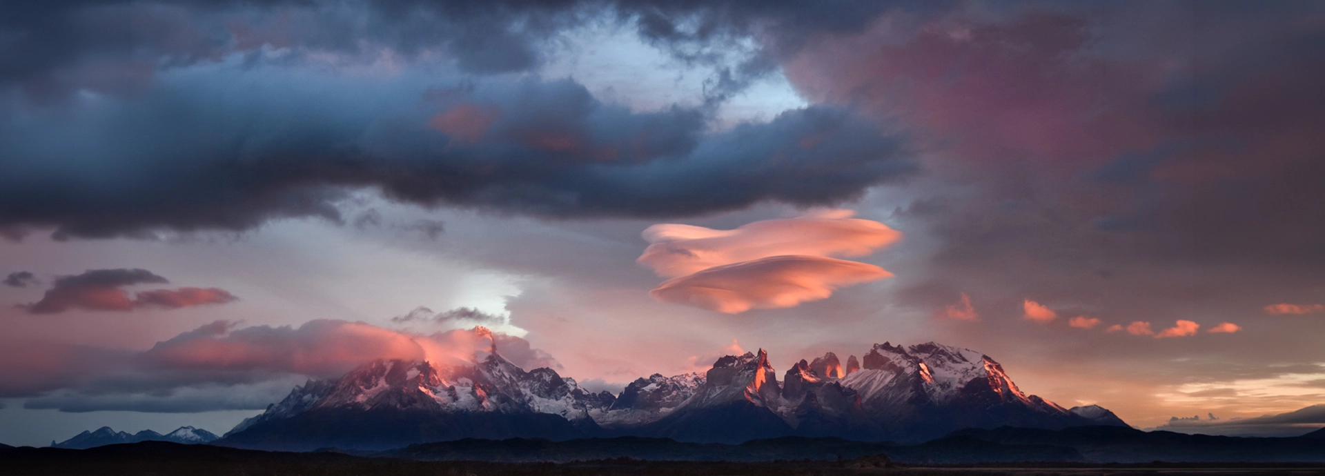 Lenticular clouds glowing pink at dusk above the jagged peaks of Torres del Paine, capturing Patagonia’s dramatic southern skies.