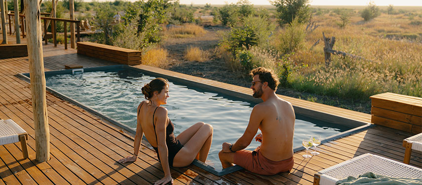 Couple sit by a lap pool and sun loungers at a luxurious safari camp in Botswana