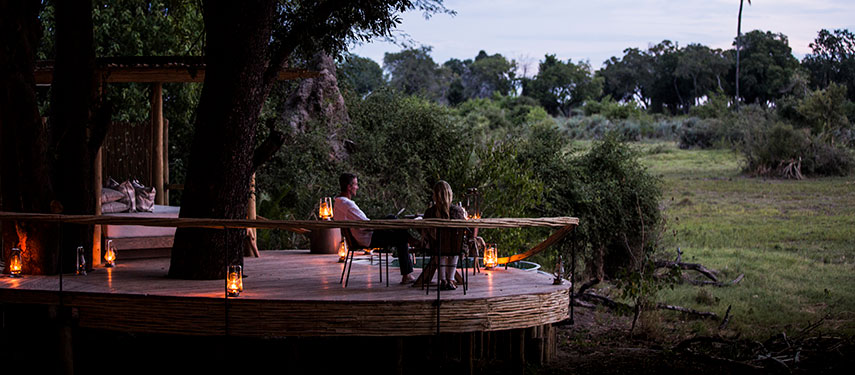 Couple enjoy sunset drinks on the deck at Mombo Camp in the Okavango Delta