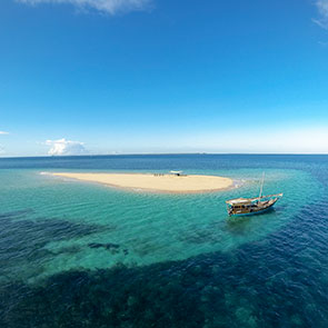 Stunning view of a couple enjoying a picnic on a sand bar with a dhow in the foreground off thew coast of Mozambique.