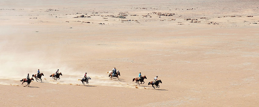Seven horse riders gallop across the desert in Namibia