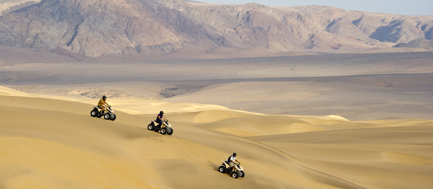 Tourists take a guided quad bike safari across sand dunes of Kaokoveld, Namibia