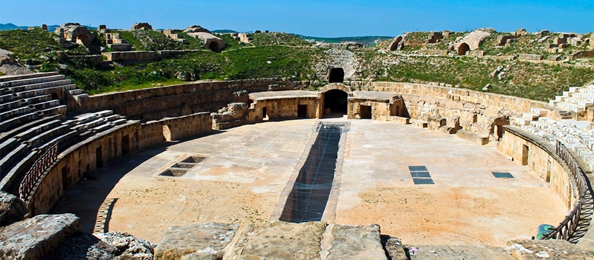 Ancient Roman amphitheatre ruins at Oudna with stone seating and open views across the surrounding hills.