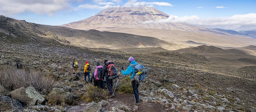 Group of trekkers navigating a rocky alpine trail with Kilimanjaro’s broad slopes visible in the background.