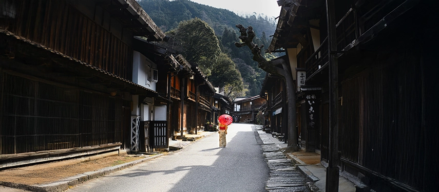 A solitary figure carrying a red umbrella walks through a preserved Edo-period street, capturing the quiet atmosphere of historic Japan.