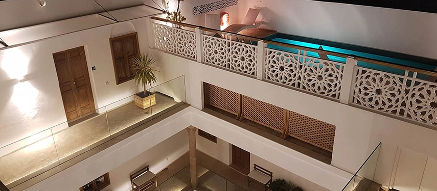 Evening view of the riad courtyard with an illuminated swimming pool on the upper level and intricate white latticework.