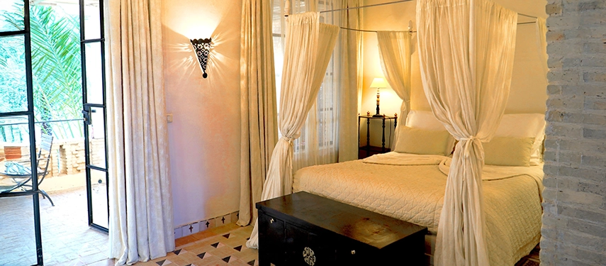 Elegant suite with white draped canopy bed, patterned floors, and terrace views at Dar Tozeur.