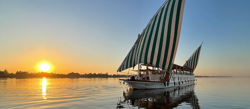 Queeny Of The Nile luxury dahabeya boat sailing on the Nile at sunset in Egypt.