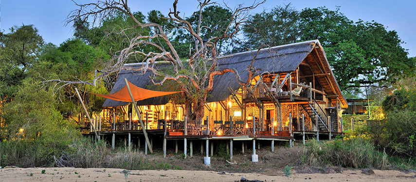 Rhino Post Safari Lodge illuminated from within as sunset descends on Kruger National Park, South Africa