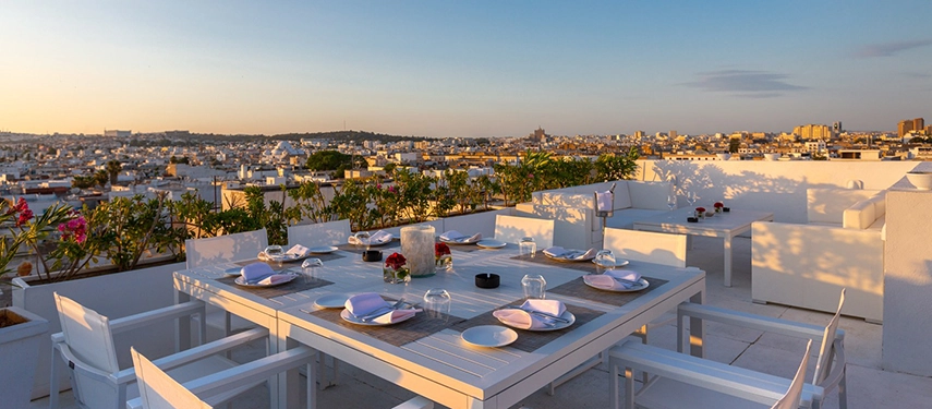 Rooftop terrace with white tables set for dinner overlooking Tunis at golden hour.