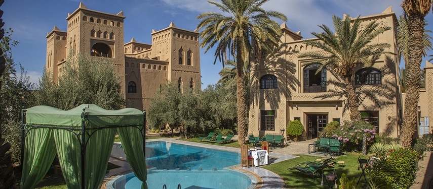 Kasbah-style pool courtyard at Ksar El Kabbaba with palm trees, shaded seating, and fortress-like towers.