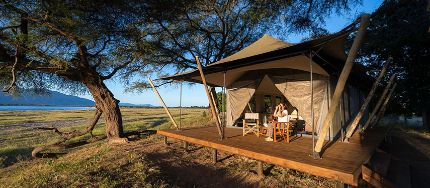 Female guest searches for game with her binoculars from her tented suite at Ruckomechi safari camp in Mana Pools National Park, Zimbabwe