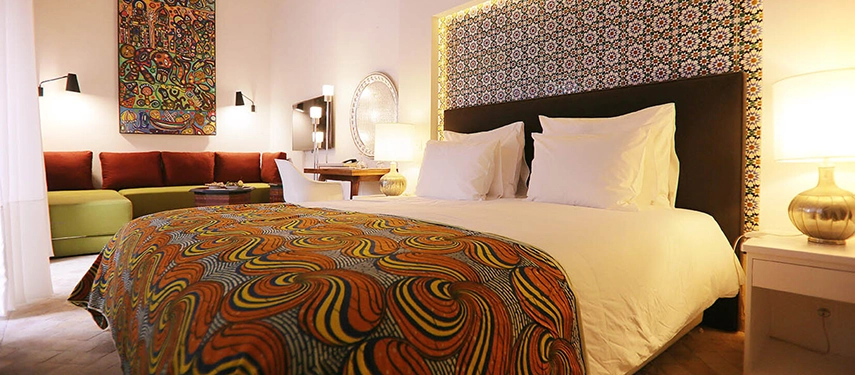 Vibrant guest room featuring patterned fabrics, colourful artwork, and a striking tiled headboard.