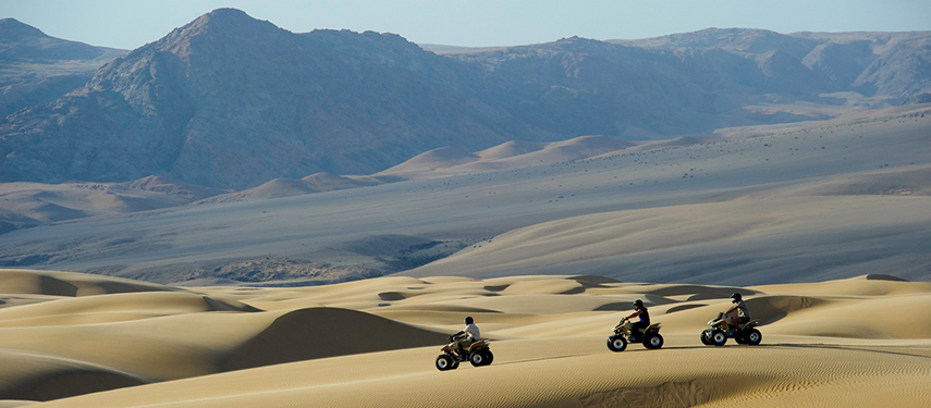 Tourists take a guided quad bike safari across sand dunes of Kaokoveld, Namibia