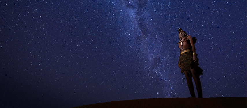 Himba tribeswoman under the spectacular, star-studded night sky of Namibia