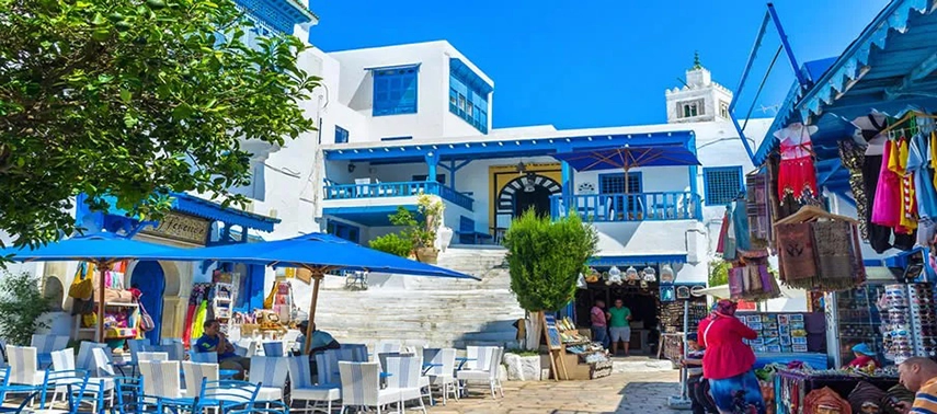Outdoor café and market square in Sidi Bou Said with blue-and-white buildings, umbrellas, and artisan stalls.