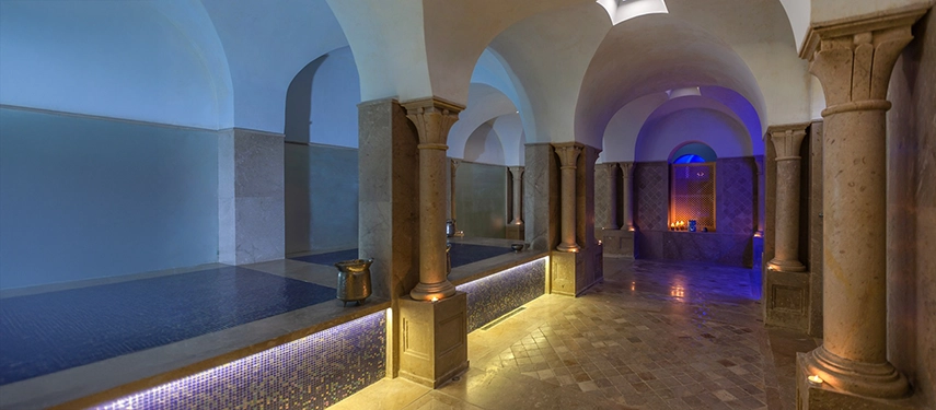Traditional hammam interior with arched stone columns, mosaic tiles, and candlelit alcoves.