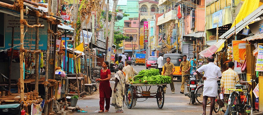 Busy street market scene in Sri Lanka with people shopping and a vendor pushing a cart of bananas.