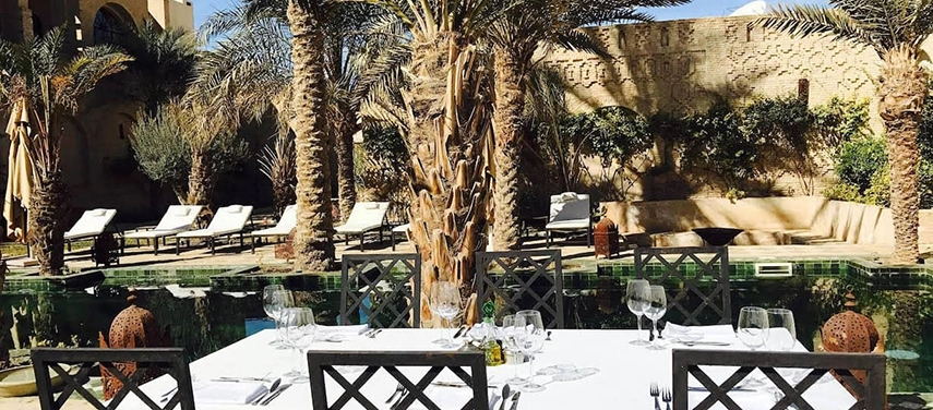 Outdoor dining table set beside the pool and palm trees at Dar Tozeur.