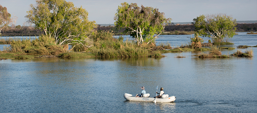 Two people canoeing through calm waters surrounded by lush river islands and greenery.