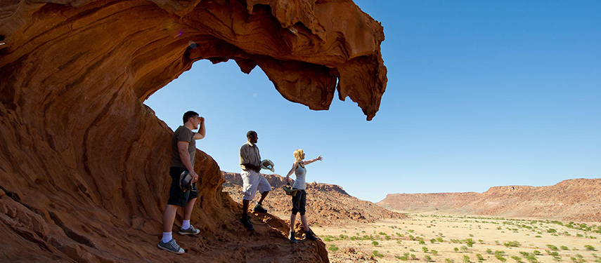 Three People Exploring Dramatic Rock Formation Desert Landscape